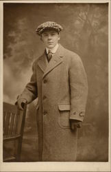 Young man in Overcoat and Cap with hand on chair Young man in Overcoat and Cap with hand on chair