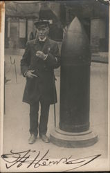 A man in a naval uniform standing beside a large shell. Postcard