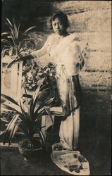Young woman in a long dress posing among potted plants Postcard