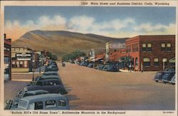 Main Street and Business District - "Buffalo Bill's Old Home Town", Rattlesnake Mountain is in the Background Postcard