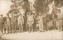 Eight men in work clothing stand in front of team of horses with equipment Postcard