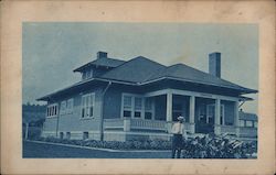 Old house with a man standing outside touching an elephant ear plant. Postcard