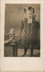 Child in Big Coat Standing next to a Doll Postcard