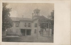 An old school house with two boys playing on a homemade wooden swing set. Postcard