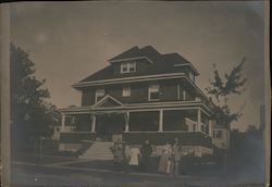 A group of people standing outside of a large house. Postcard
