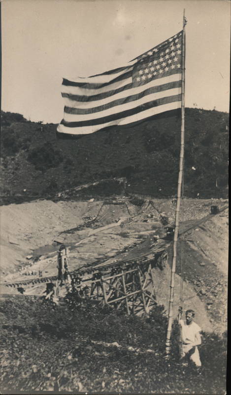 Man Stands by American Flag, Dam or Canal Construction?