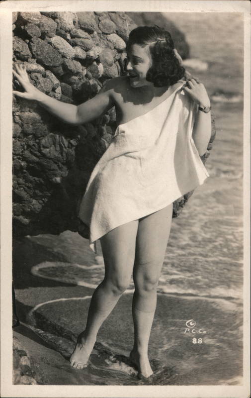 Flapper Woman covering herself in a towl by an ocean rock