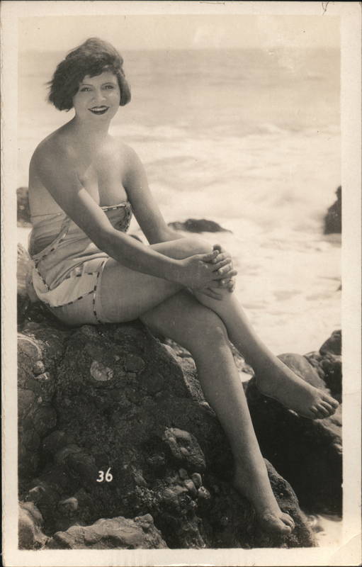 Flapper Woman in bathing attire sitting on Rocks by the Ocean