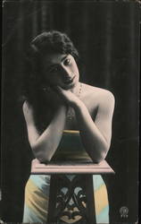 Woman in yellow and blue striped dress rests her elbows on a small table Postcard