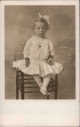 Young Girl with Bow in Hair Seated on Wooden Chair Postcard