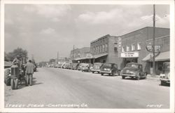 Main Street with Fort Theater, Stewart Drug, Oscar's Department Store, and parked cars Postcard