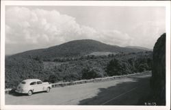 Car parked on mountain road with scenic view and cloudy sky Postcard