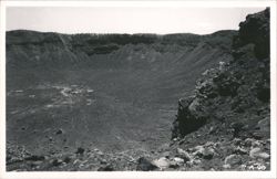 View of a large meteor crater with buildings at the base Postcard