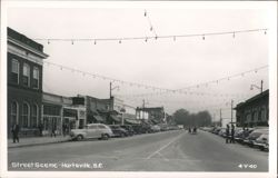Downtown Street Scene with Parked Cars and String Lights Postcard