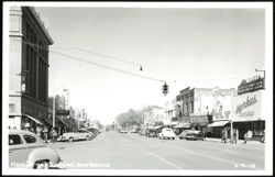 Main Street with numerous cars and storefronts Postcard