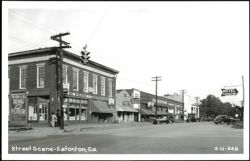 Downtown street scene with businesses and parked cars Postcard