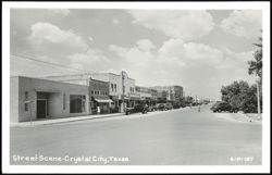 Downtown street scene with businesses and parked cars Postcard
