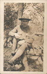 Man in Hat & Uniform Sitting on Log Fence Postcard