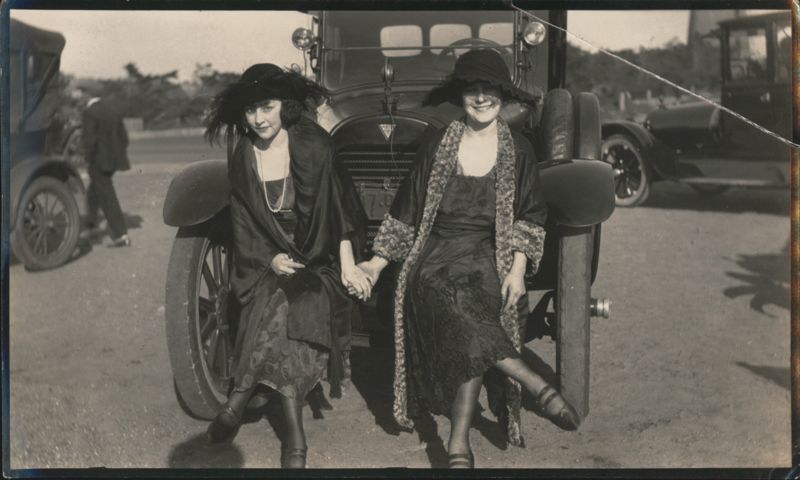 Two Women in 1920s Fashion Sitting on Vintage Car Bumper