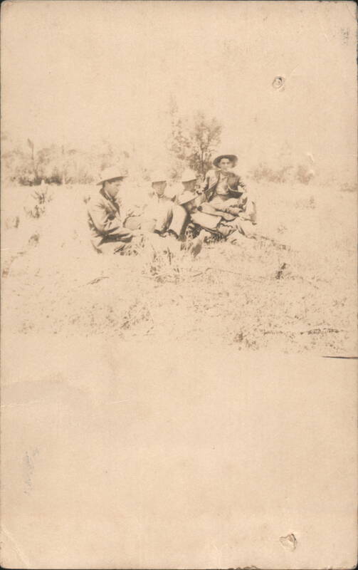Group of Five Men Seated in Grassy Field Wearing Hats
