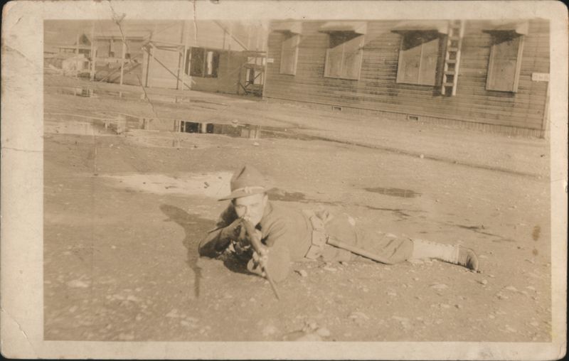 WWI Soldier Prone Aiming Rifle at Camera, Military Camp