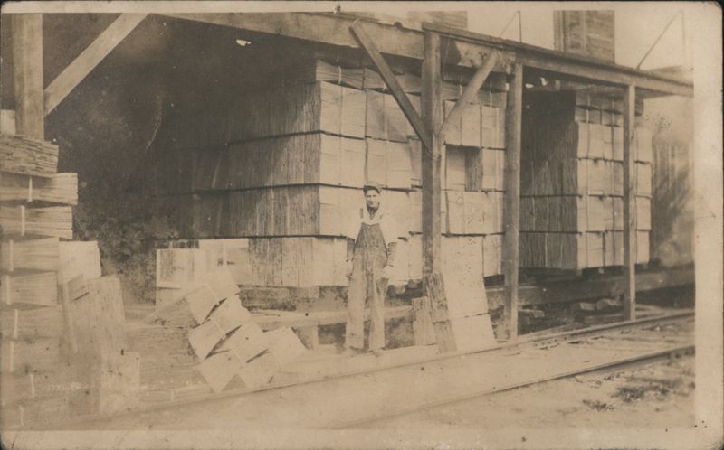 Lumber Yard Worker Standing by Stacks at Rail Siding