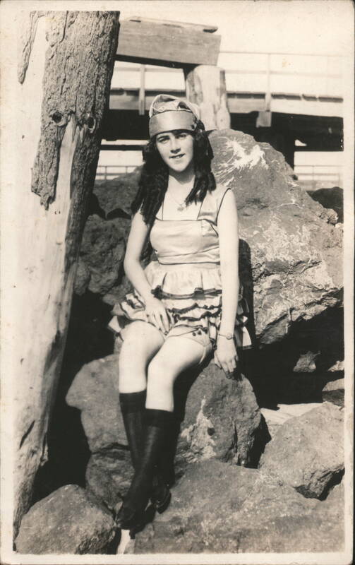 Flapper Woman in Ruffled Swimsuit Reclining on Rocks by Pier