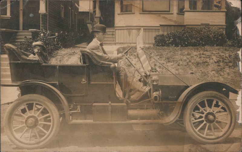 Man in Bowler Hat Driving Early Automobile with Child 1910