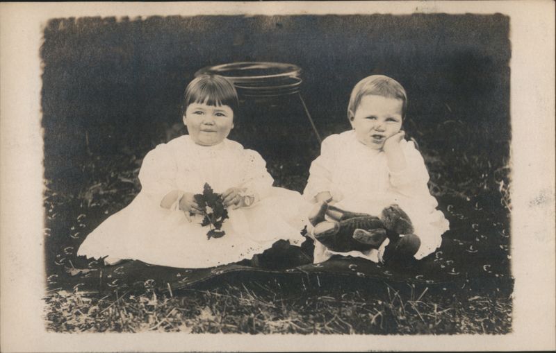 Two Toddlers in White Dresses with Teddy Bear on Blanket