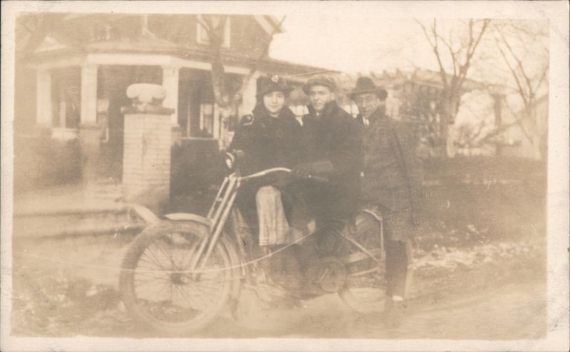 Three people with motorcycle by house Motorcycles