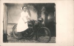 Nurse in white dress on early motorcycle, tropical setting Postcard