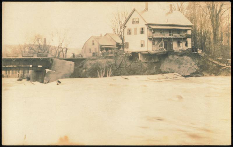 Flood Waters Eroding Riverbank Near Bridge and Houses