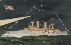 US Navy Battleship Illuminated at Night with Flags and Searchlight Postcard