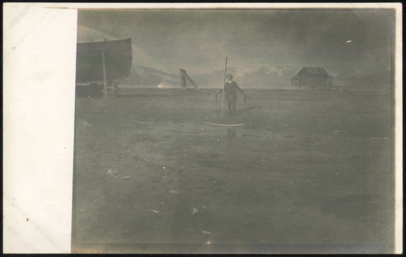 Man with Pole, Boats, Building on Stilts, Mountains