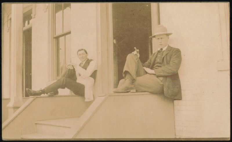 Two Men Sitting on Steps, One in Hat & Suit, One in Vest & Glasses