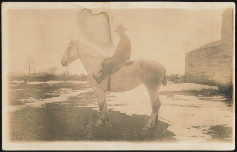 Man on Horseback in Snowy Field with Barn Horses