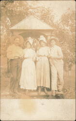 Four People in Hats by Wooden Structure Postcard