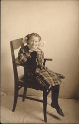 Girl in plaid dress sitting on a chair Postcard