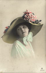 Woman Wearing White Dress Trimmed in Green and Big Straw Hat With Pink and White Flowers Postcard