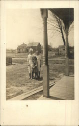 Family photo of three girls in front of their home in the early 20th century Postcard