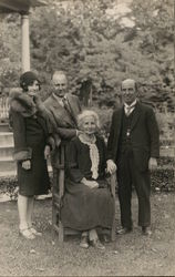 A Woman Sitting in a Chair with Three People Standing Around Her Postcard