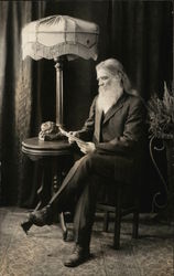 Man with White Beard Reading While Seated Near Table, Lamp Postcard