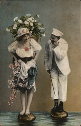 Woman with flowers stands next to man on stones in the water Postcard
