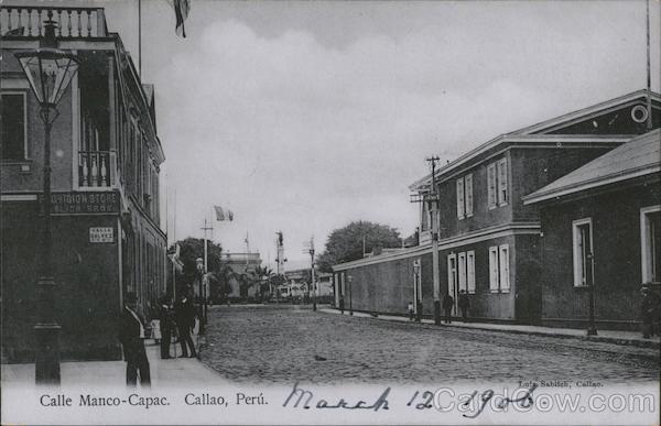 Cobblestone street lined with two-story buildings, utility poles with pedestrians Callao Peru