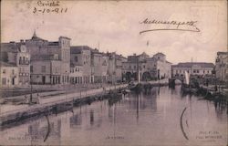 A canal with boats lined by roads and buildings Postcard