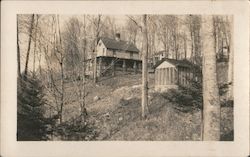 2 story home on a hill in the woods with a shed and trees Postcard