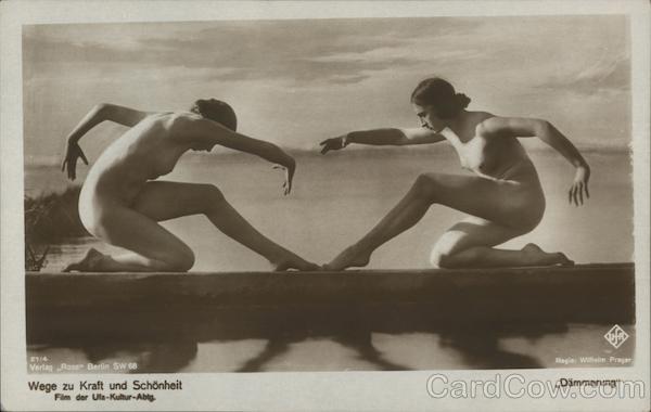 Two nude women posing as if dancers or statues on a platform over a lake
