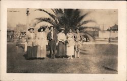 Group photo in front of palm tree, one man in uniform Postcard