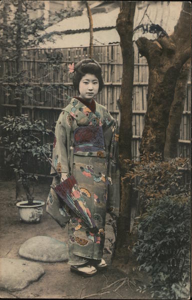 Japanese geisha standing beside tree holding a parasol