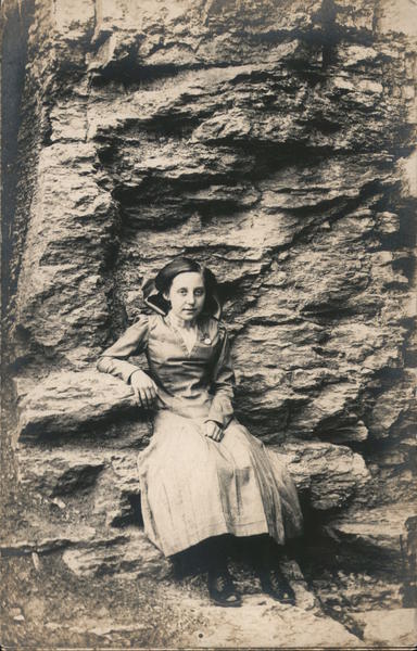 Girl with watch pin on dress sitting on natural cliff seat.
